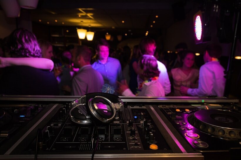 Dynamische Party-Szene mit DJ, Mischpult, Kopfhörern und beeindruckender Beleuchtung in der Disko – perfekte Atmosphäre zum Tanzen und Feiern