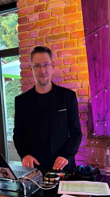 Auf diesem Bild steht DJ Stefan Masur am Rand der Tanzfläche und beobachtet, wie das Brautpaar den Eröffnungstanz genießt. Im Hintergrund ist seine gesamte Anlage zu sehen – von den Lautsprechern über das Mischpult bis hin zur stimmungsvollen Beleuchtung.